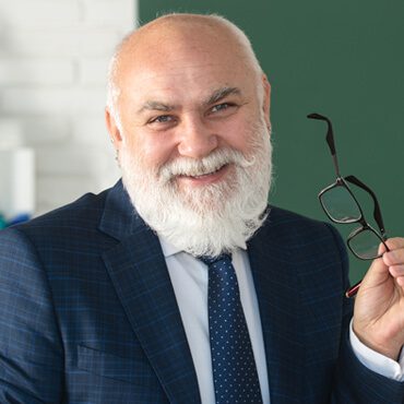 A man in a suit holding glasses and smiling.