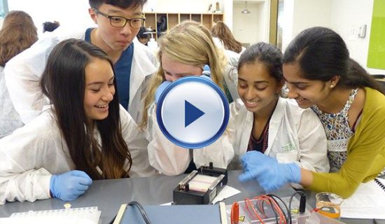 A group of students in lab coats looking at an electronic device.