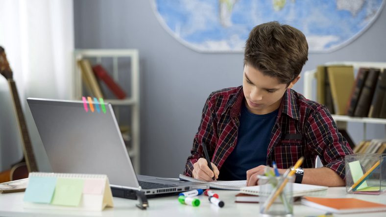 A boy is writing on paper at the table